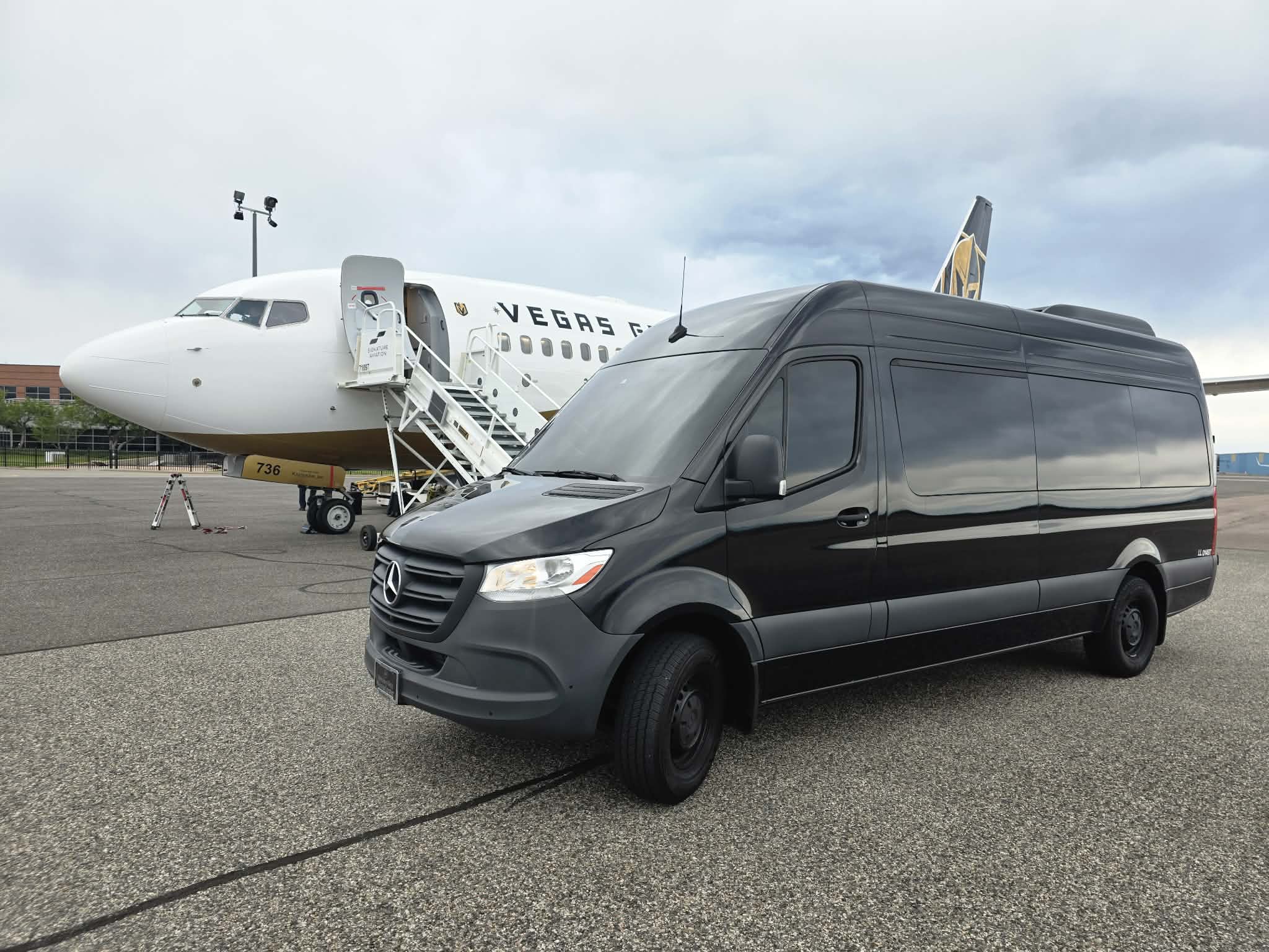 Black Mercedes-Benz Sprinter van on the tarmac beside a private jet at a Colorado FBO