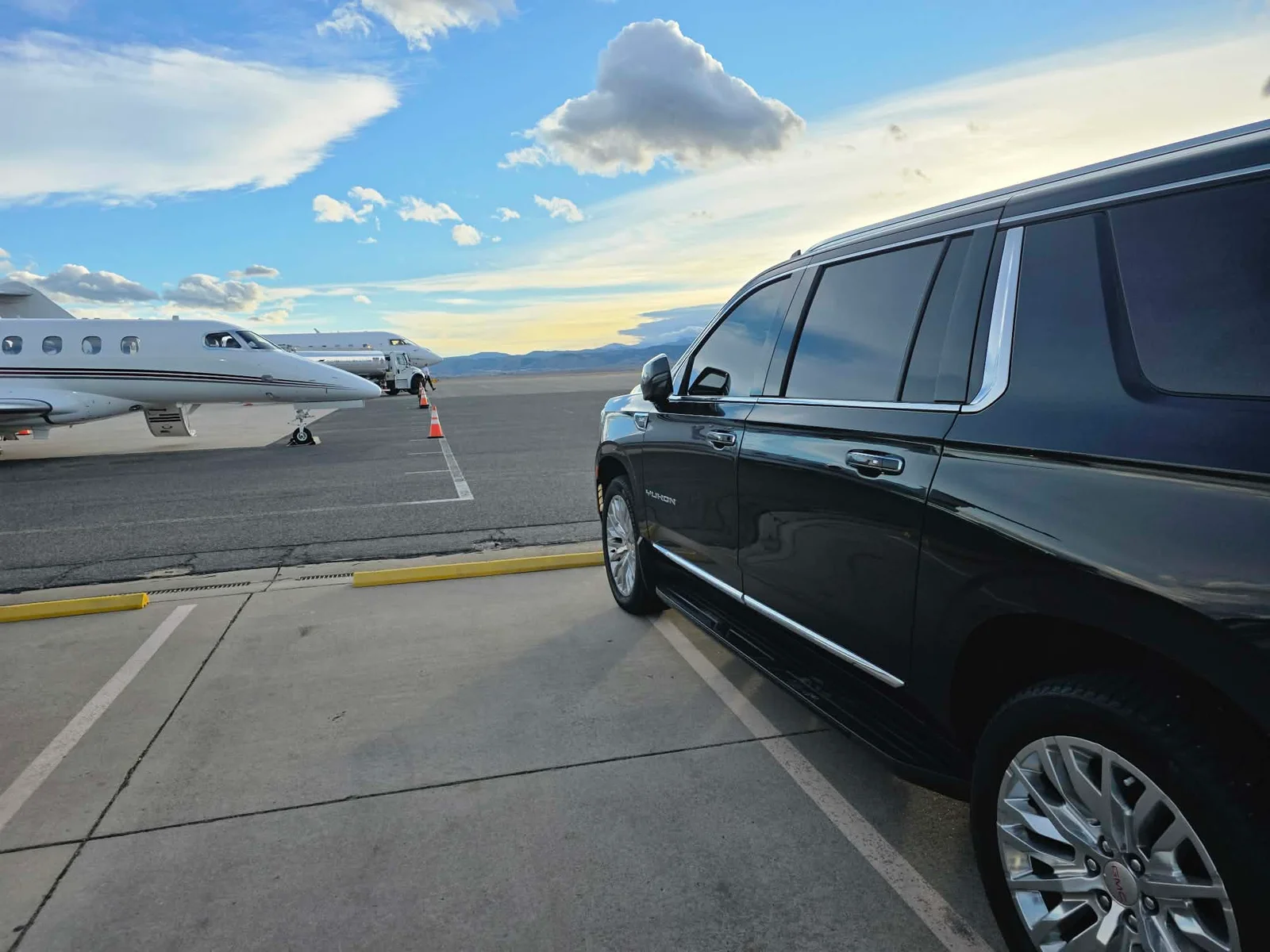 Black GMC Yukon at a Colorado FBO with private jets and the Rockies behind it